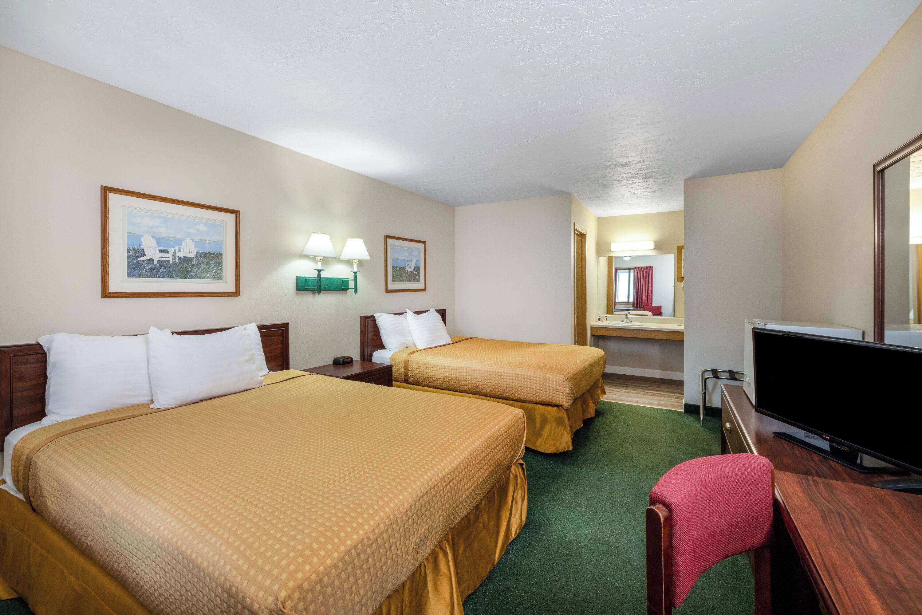 Habitación de hotel con dos camas, un escritorio, televisión y baño a la vista.