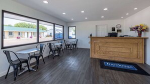 A reception area with a wooden desk, a black reception mat, and a view of the outside. - Travelodge by Wyndham Spirit Lake/Okoboji (Spirit Lake)