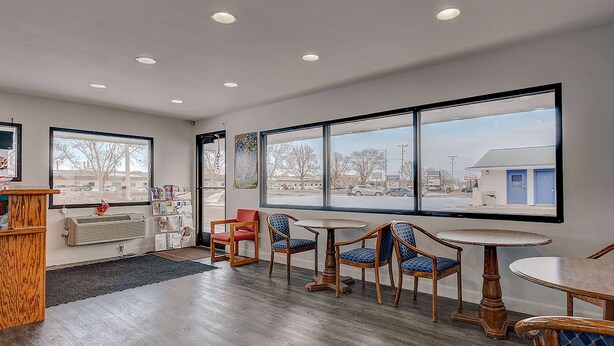 A spacious room with large windows, a wooden reception desk, and a seating area with chairs and a table. - Travelodge by Wyndham Spirit Lake/Okoboji (Spirit Lake)