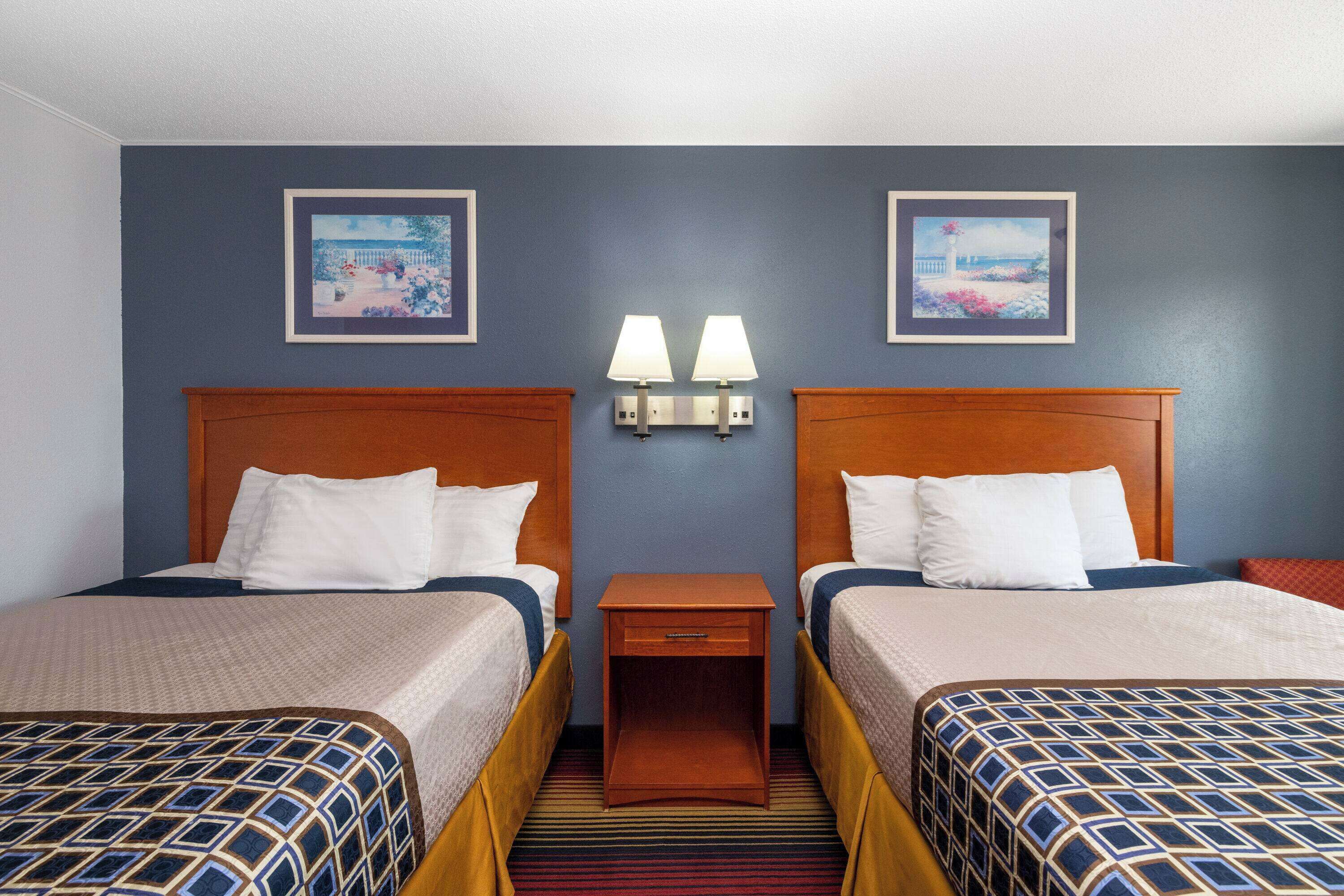 A hotel room with two beds, a nightstand with lamps, and two framed pictures on the wall.