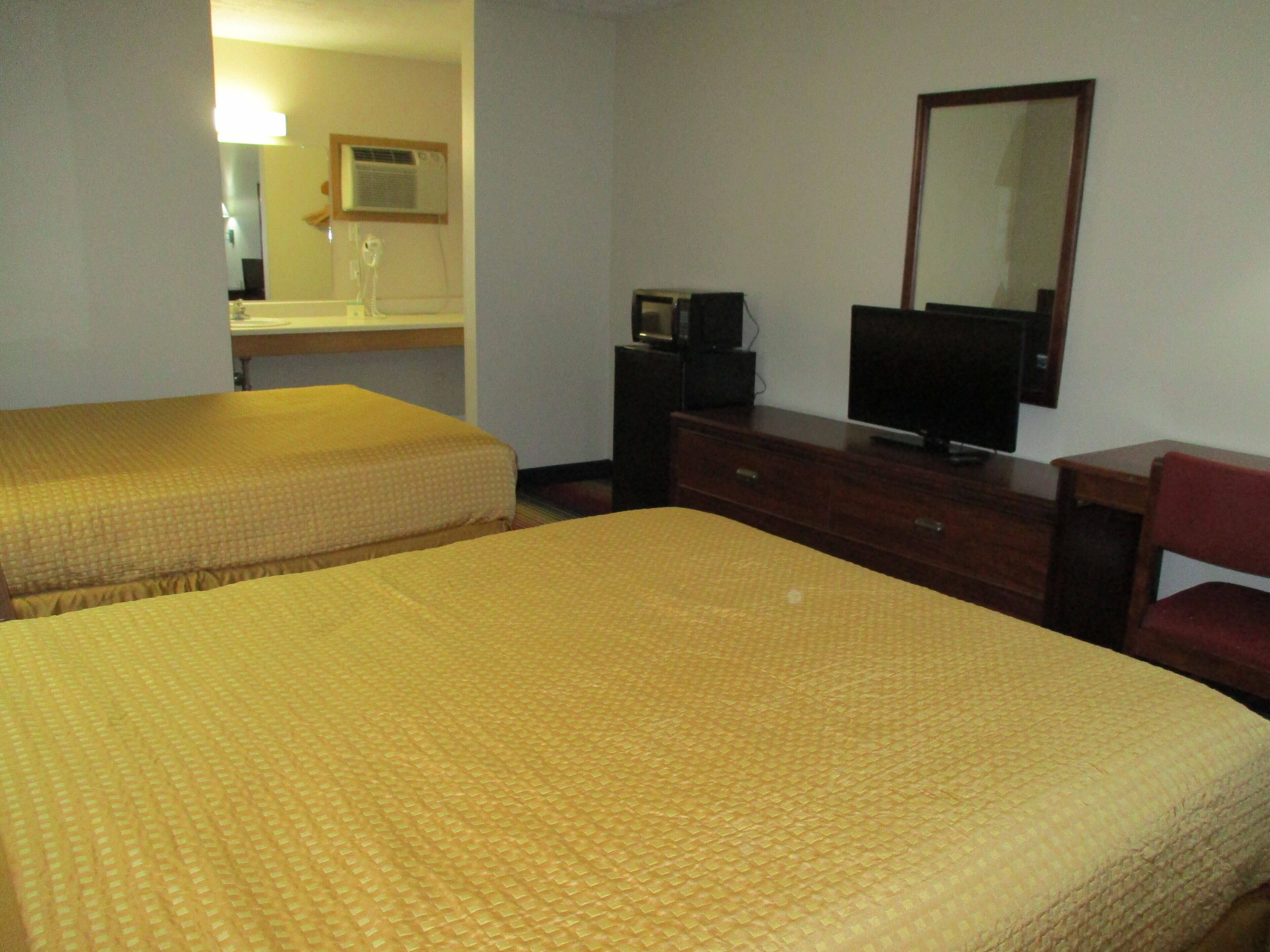 A hotel room with two beds, a dresser, a television, and a mirror.