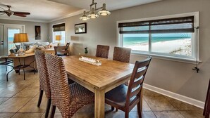 A dining area with a wooden table and wicker chairs, a ceiling fan, and a view of the beach through a window with blinds. - 20 Sanddollar 3 Bedroom Holiday Home by Five Star Properties (Miramar Beach)