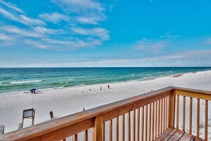 Vista a la playa desde una terraza de madera, cielo despejado y océano.