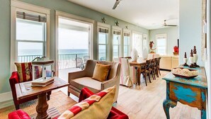 Ein großzügiger Wohnbereich mit großem Fenster zum Meer, einem Deckenventilator und einem Essbereich mit Tisch und Stühlen.