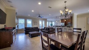 A spacious living room with a large wooden dining table, dark sofas, and a kitchen area with modern appliances. - Acqualina 9 Bedroom Holiday Home by Five Star Properties (Miramar Beach)