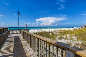 A wooden boardwalk leading to a beach with a flag, clear skies, and a calm sea.