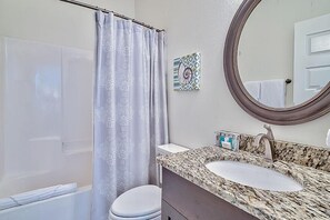 Une salle de bain avec un rideau de douche, un lavabo doté d’un plan de travail en marbre, des toilettes et un miroir.