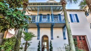 Un bâtiment à deux étages doté d’un balcon, d’une arche centrale et de plantes en pot disposées autour de l’entrée.