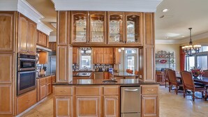 A spacious kitchen with wooden cabinetry, a central island, and a dining area with chairs and a table. - Bella Luna 4 Bedroom Holiday Home by Five Star Properties (Destin)