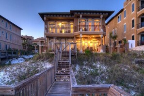 A multi-story building with a wooden deck leading to a balcony, surrounded by sand dunes.