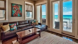 A living room with a dark leather sofa, a wooden coffee table, and a large window offering a view of the ocean. - Bella Vizio 5 Bedroom Holiday Home by Five Star Properties (Miramar Beach)