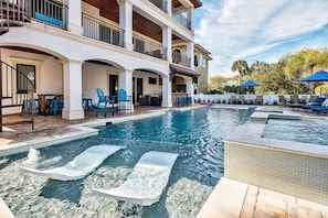 A multi-story hotel with a swimming pool, outdoor seating, and a view of palm trees. - Big House by the Sea 8 Bedroom Holiday Home by Five Star Properties (Destin)