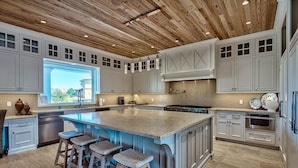 A spacious kitchen with a large island, white cabinetry, and a wooden ceiling.