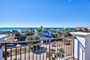 A coastal view from a balcony overlooking a resort area with multiple buildings, palm trees, and a clear blue sky. - Big House by the Sea 8 Bedroom Holiday Home by Five Star Properties (Destin)