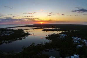A sunset over a calm lake with a distant shoreline and a few buildings.