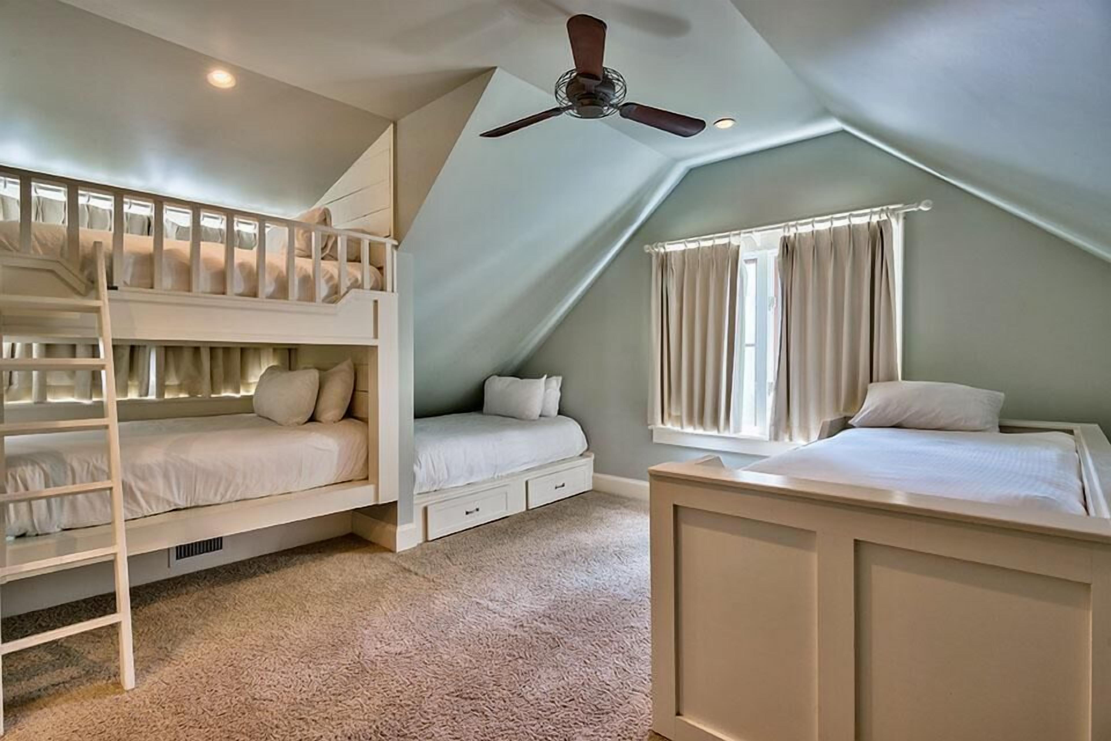 A dorm-style room with bunk beds, a desk, and a window with curtains.