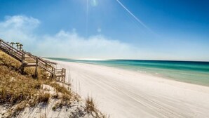 A beach with a wooden staircase leading down to the sand, clear blue sky, and calm ocean.