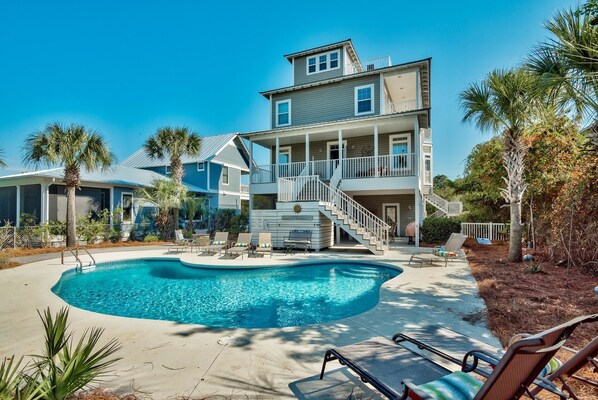 A two-story house with a swimming pool, outdoor seating, and a staircase leading to a balcony.