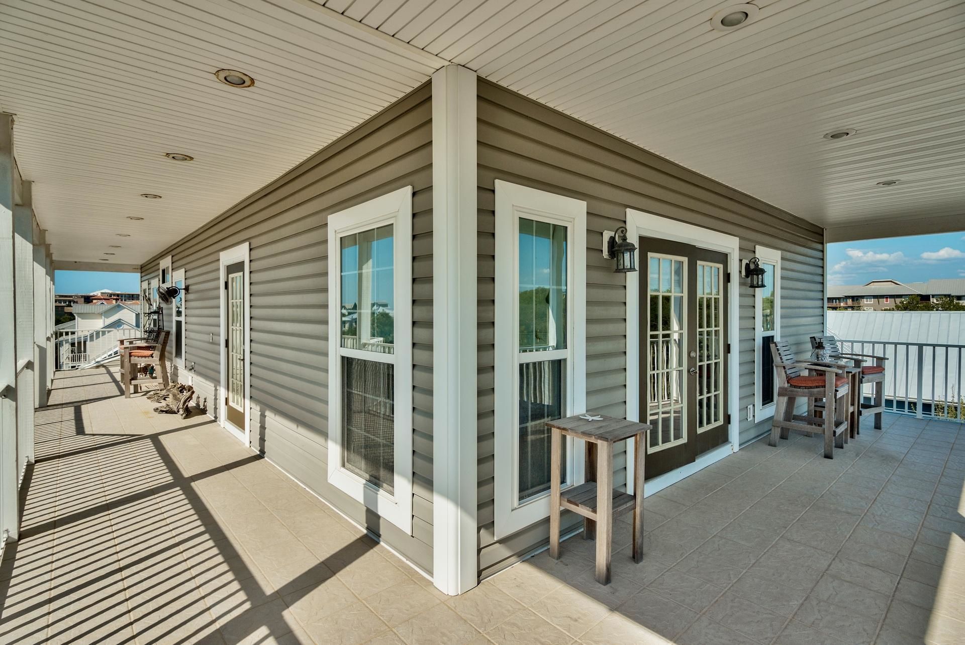 A covered porch with a wooden table and chairs, a small table, and a railing.