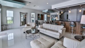 A modern living room with a large sofa, a coffee table, and a kitchen area with bar stools. - Bord du Mer 6 Bedroom Holiday Home by Five Star Properties (Miramar Beach)