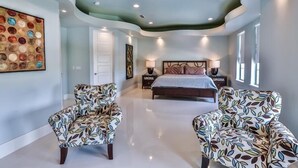Quarto com teto arredondado, uma cama, duas mesas de cabeceira e duas poltronas estampadas.