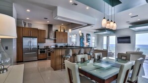 A modern kitchen with a central island, stainless steel appliances, and a dining area with a glass table and chairs. - Bord du Mer 6 Bedroom Holiday Home by Five Star Properties (Miramar Beach)