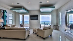 A spacious living room with a large sofa, a smaller sofa, and a coffee table. There is a flat-screen TV mounted on the wall, and large windows offering a view of the ocean. - Bord du Mer 6 Bedroom Holiday Home by Five Star Properties (Miramar Beach)