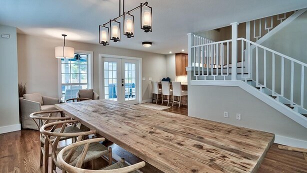 A spacious kitchen with a long wooden table, white railing staircase, and large windows. - Bottoms Up 7 Bedroom Holiday Home by Five Star Properties (Destin)