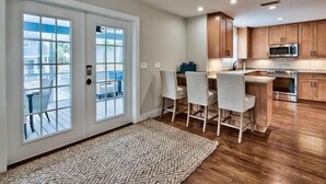 A modern kitchen with wooden cabinets, a stainless steel microwave, and a built-in oven. There is a dining area with a table and chairs, and a large window with a view of the outside. - Bottoms Up 7 Bedroom Holiday Home by Five Star Properties (Destin)