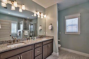 A bathroom with a granite countertop, dark wooden cabinets, a large mirror, and a window with blinds. - Camino de la Playa 4 Bedroom Holiday Home by Five Star Properties (Santa Rosa Beach)