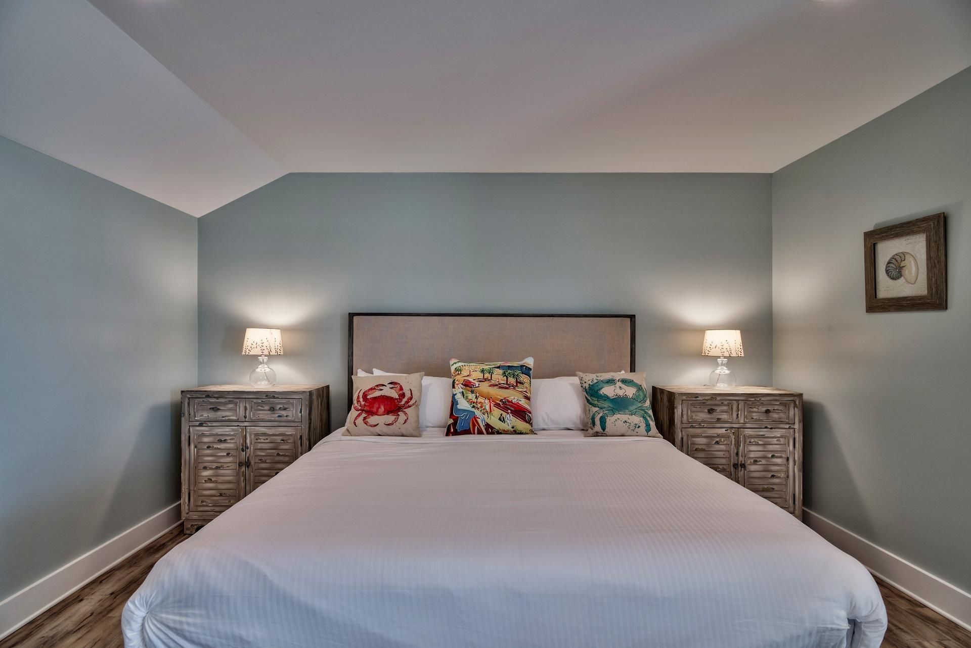 A bedroom with a large bed, two bedside tables with lamps, and a framed picture on the wall.