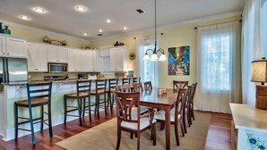 Une cuisine avec des meubles blancs, une table à manger avec des chaises et un luminaire suspendu.
