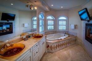 Une salle de bain spacieuse dotée d’un grand lavabo ovale, d’une baignoire sur pieds et de trois fenêtres en arc qui laissent entrer la lumière naturelle.
