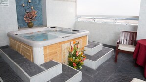 Een wellnessruimte met een jacuzzi, houten treden, een stoel en een tafel.
