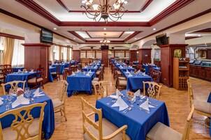 A banquet hall with rows of tables set for dining, wooden chairs, and a wine rack.