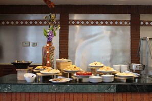 Montaje de bufé con diversos alimentos y un jarrón decorativo.