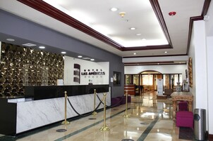 A hotel reception area with a marble counter, gold stanchions, and a sign for 'Hotel Las Americas'.