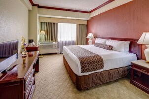 Ein Hotelzimmer mit einem großen Bett, einem Fernseher, einem Schreibtisch und einem Fenster mit Vorhängen.