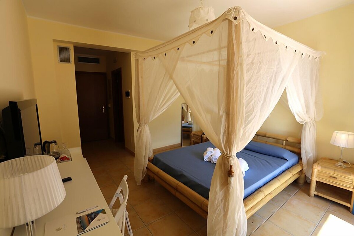 A room with a four-poster bed, a desk with a lamp, and a bedside table.