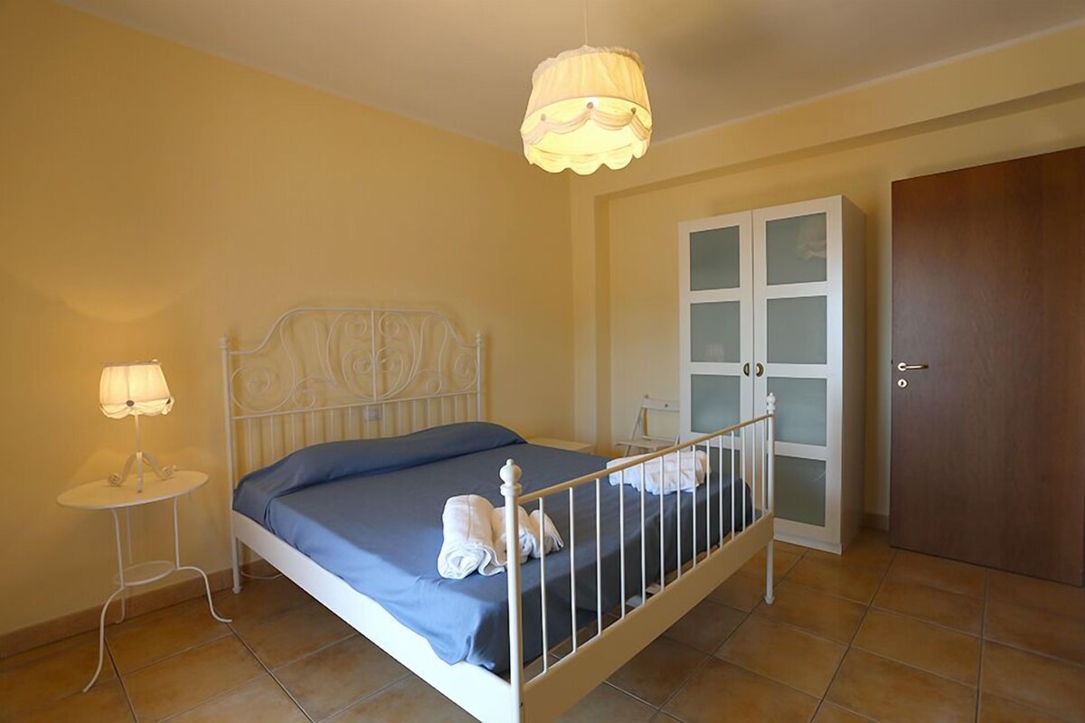 A bedroom with a bed, bedside table, lamp, wardrobe, and a door.