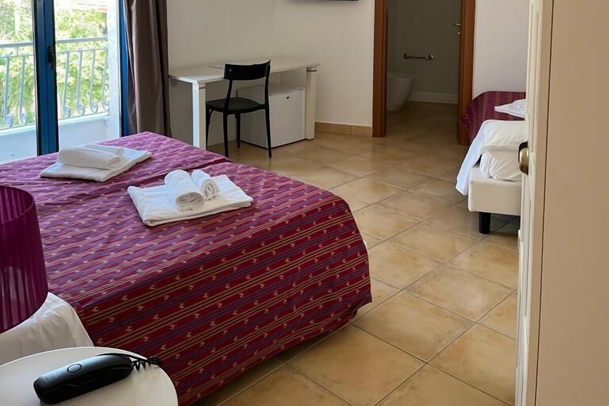 A hotel room with a bed, a desk, a chair, a TV, and a balcony.