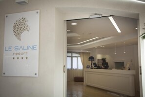 A reception area with a sign for Le Saline Resort, a reception desk, and a view into the room. - Le Saline Resort (Montebello Ionico)