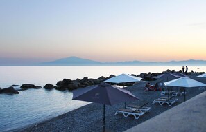 A beach with umbrellas and lounge chairs, rocky shoreline, and a calm sea. - Le Saline Resort (Montebello Ionico)