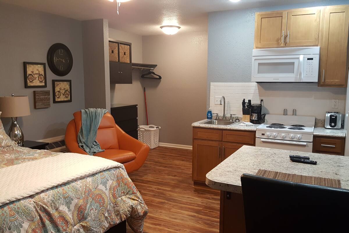 A compact living space with a bed, a chair, a kitchenette, and a dining area.
