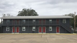 Un motel de dos pisos con techo plano, varias puertas rojas y una escalera central.