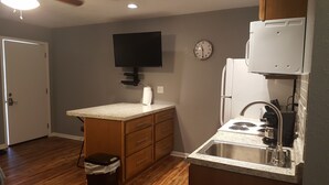 Una cocina compacta con armarios de madera, estufa empotrada, lavamanos y televisión montada en la pared.