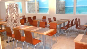 A dining area with tables and chairs, large windows with a view of the sea, and a decorative wooden structure. - Sweet Home Appart Hotel Deauville Sud (Saint-Arnoult)