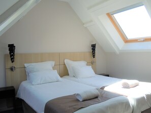 A bedroom with two beds, a skylight, and a wooden headboard. - Sweet Home Appart Hotel Deauville Sud (Saint-Arnoult)