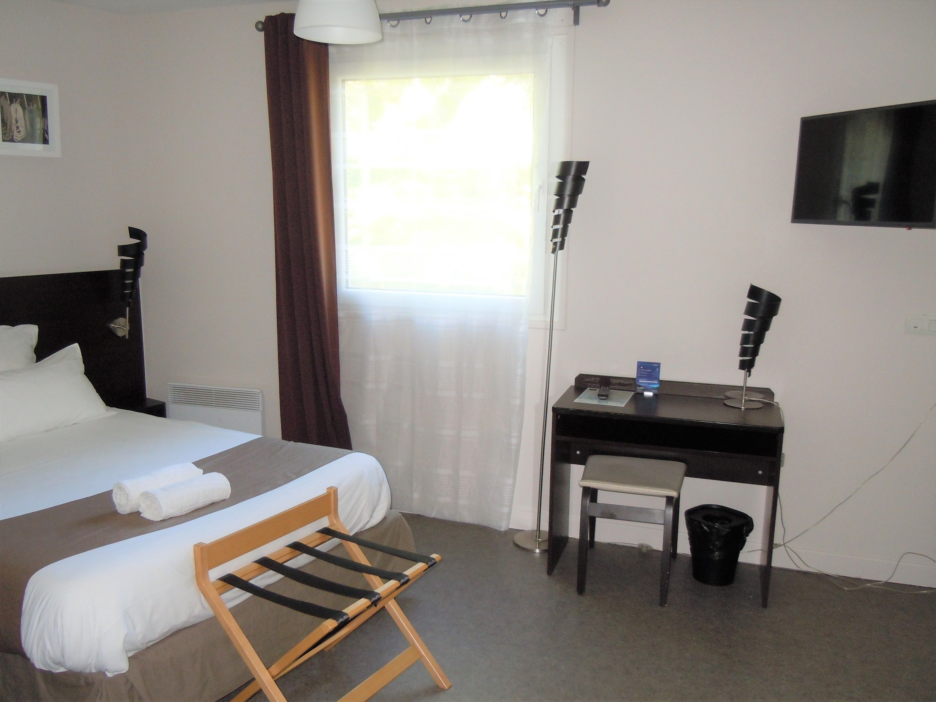 A hotel room with a bed, a desk, a chair, a lamp, and a window with curtains.