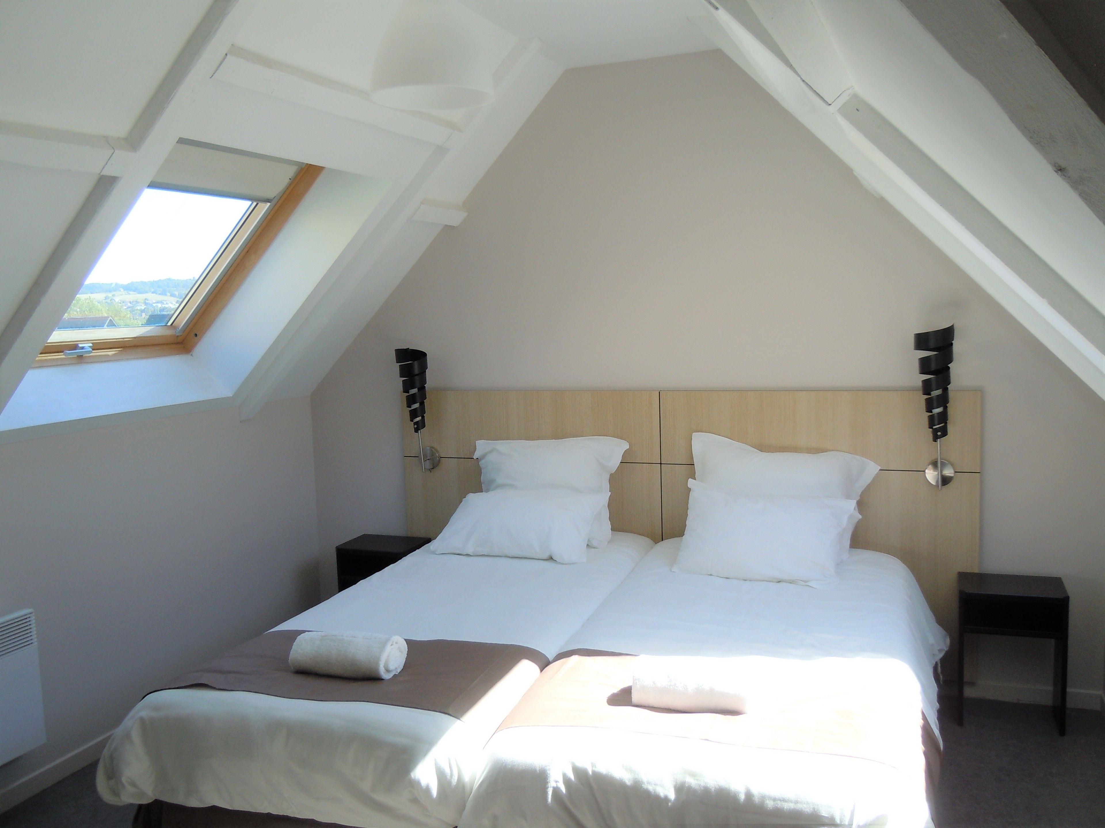 Une chambre avec deux lits, une lucarne et une tête de lit en bois.